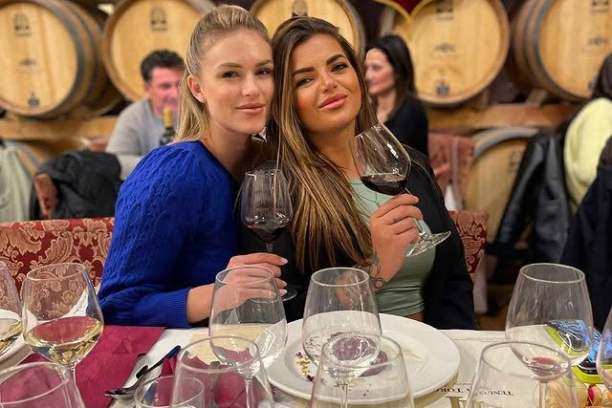 Two women sitting at table with wine glasses in a winery setting.