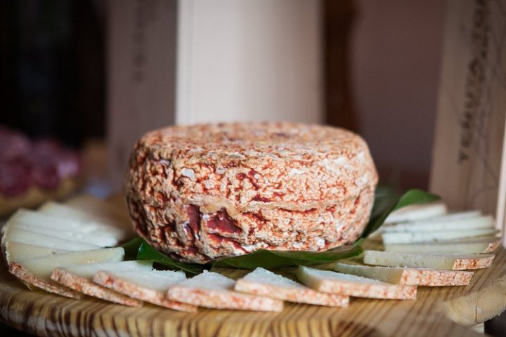 Round cheese wheel with sliced pieces on a wooden platter.