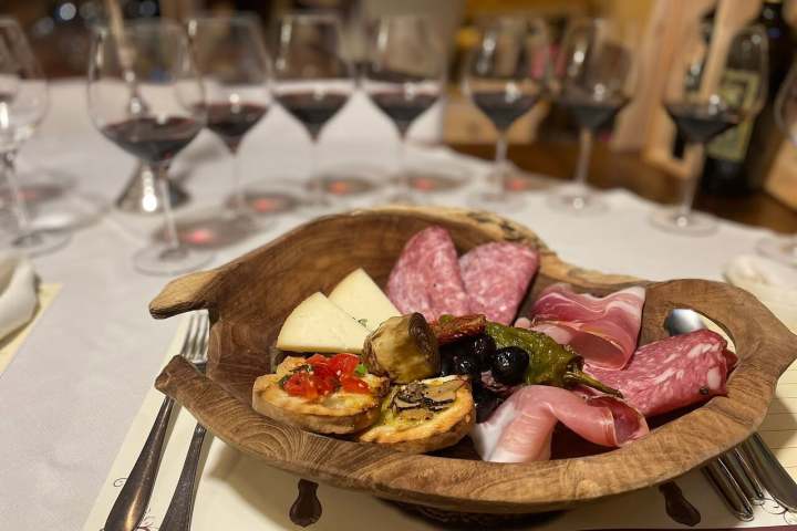 Wooden platter with meats, cheese, and bread. Glasses of red wine in the background.