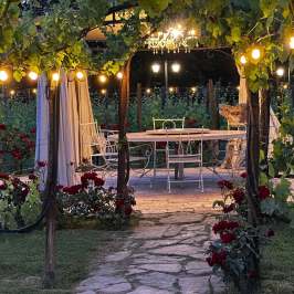 Garden patio with string lights, table, and chairs under a pergola draped with vines.