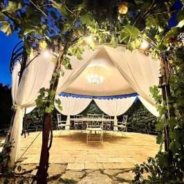 Gazebo with lights and draped fabric at night, surrounded by greenery.