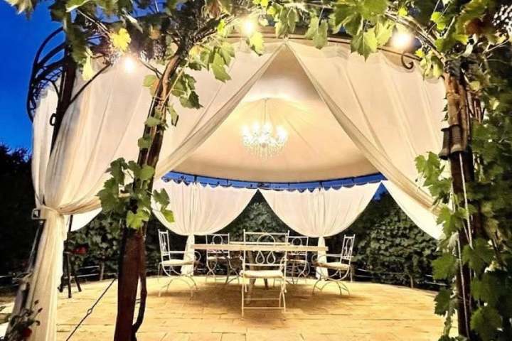Gazebo with lights and draped fabric at night, surrounded by greenery.