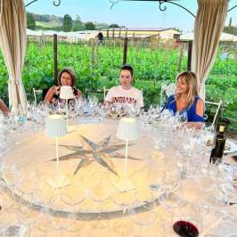 People dining at a round table set with glasses in a vineyard setting.
