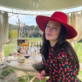 Woman in red hat holding wine glass at outdoor table with drinks.