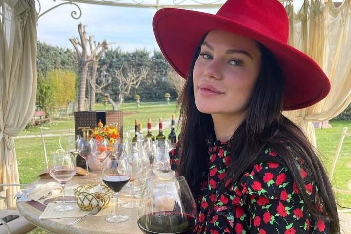 Woman in red hat holding wine glass at outdoor table with drinks.