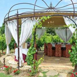 Elegant gazebo with white curtains, surrounded by greenery, set up for dining.