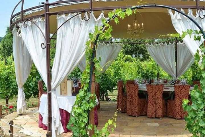 Elegant gazebo with white curtains, surrounded by greenery, set up for dining.
