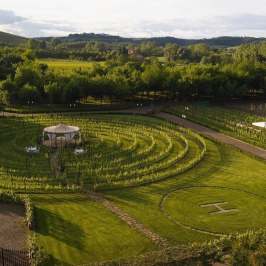 Aerial view of circular garden with paths and central gazebo, surrounded by trees and hills.