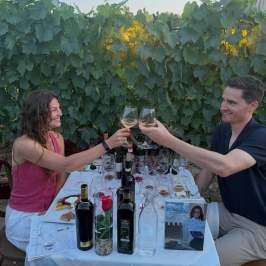 A couple toasting wine glasses at an outdoor vineyard table.