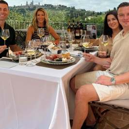 Four people dining outdoors with wine and gourmet food.