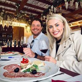 Two people smiling with wine glasses at a table with charcuterie.