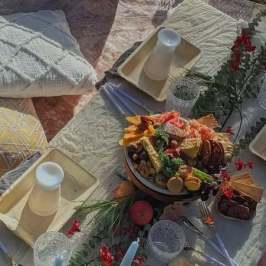 Picnic setup with food, drinks, pillows, and floral decor on a table.