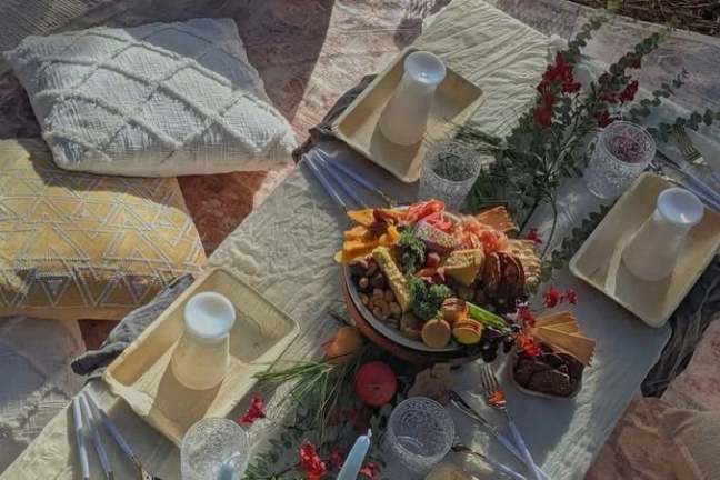 Picnic setup with food, drinks, pillows, and floral decor on a table.