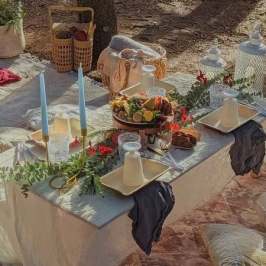 Outdoor picnic setting with table, candles, fruit platter, and drinks.