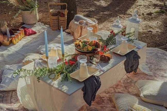 Outdoor picnic setting with table, candles, fruit platter, and drinks.