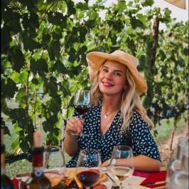 Woman in hat enjoying wine at vineyard table with food.