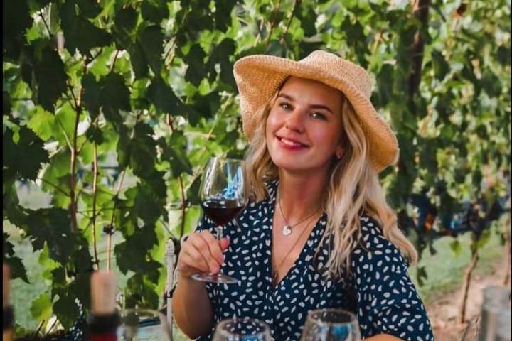 Woman in hat enjoying wine at vineyard table with food.