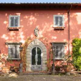 Pink Tuscan villa facade with arched door and lemon pots in Chianti