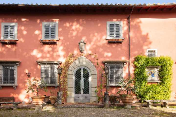 Pink Tuscan villa facade with arched door and lemon pots in Chianti
