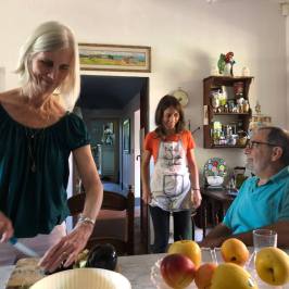 Host preparing bruschetta in a Tuscan farmhouse kitchen with guests