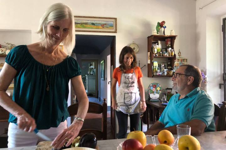 Host preparing bruschetta in a Tuscan farmhouse kitchen with guests