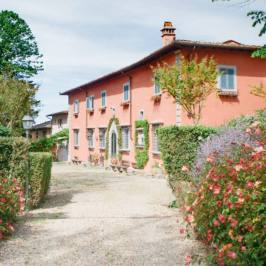 Gravel driveway with flowers leading to a pink Tuscan villa in Chianti
